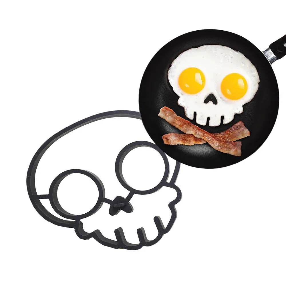 Dark skull-shaped egg mould beside a frying pan containing skull-shaped eggs with two yellow yolk eyes